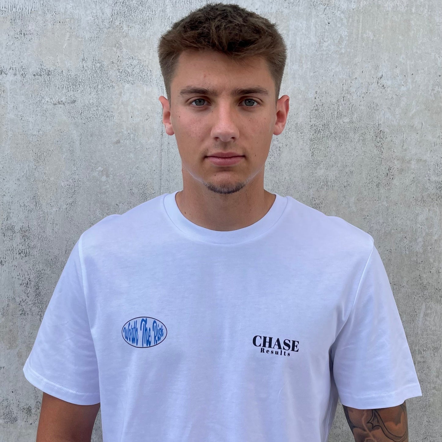 Person wearing a white t-shirt with 'CHASE' branding against a concrete wall.