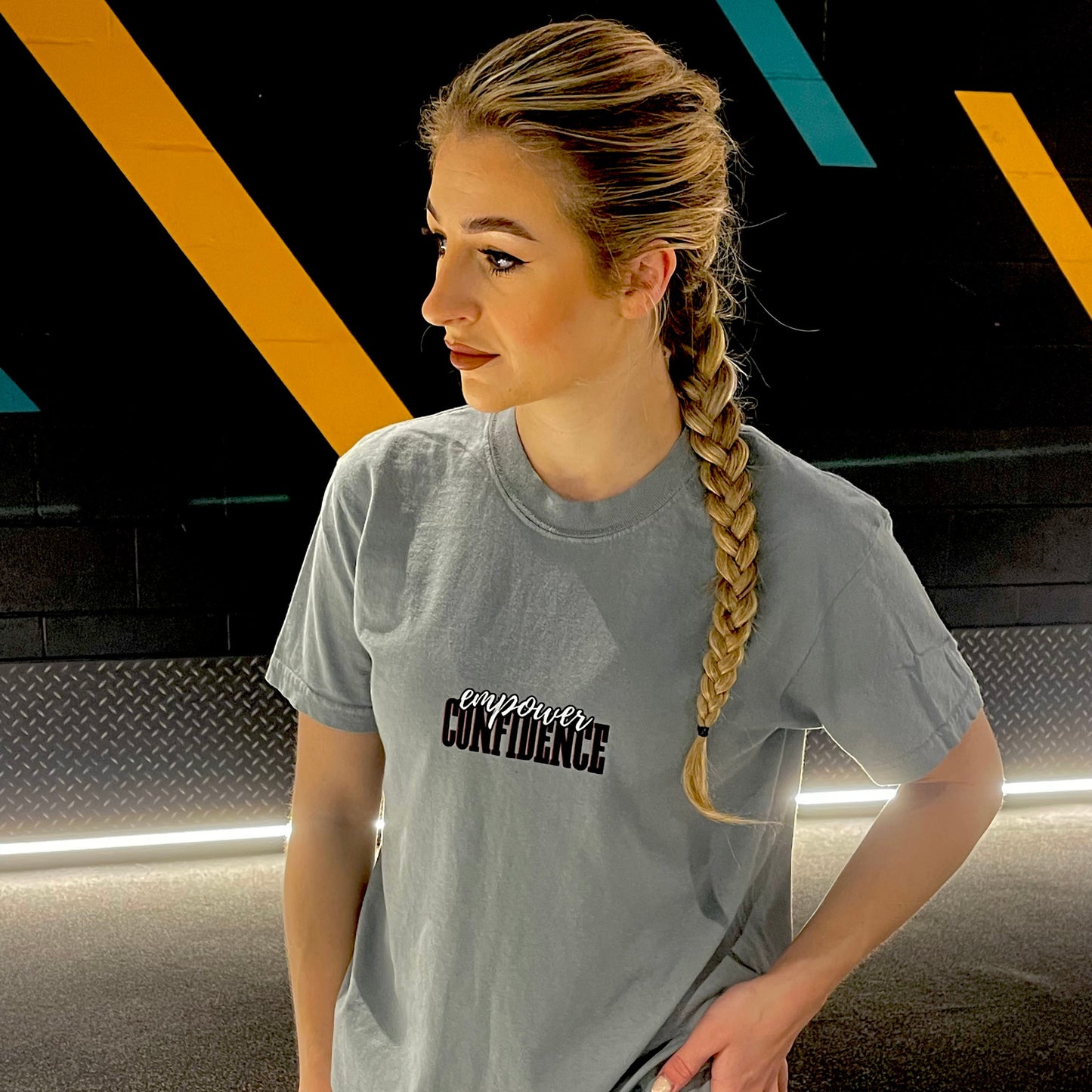 Chase Results clothing brand, based in a gym in Norfolk Norwich, features a confident girl standing in front of a dark backdrop, wearing the Empower Confidence t-shirt. The t-shirt’s bold design highlights her self-assurance, capturing a moment of strength and empowerment as she embraces her reflection with confidence and style.