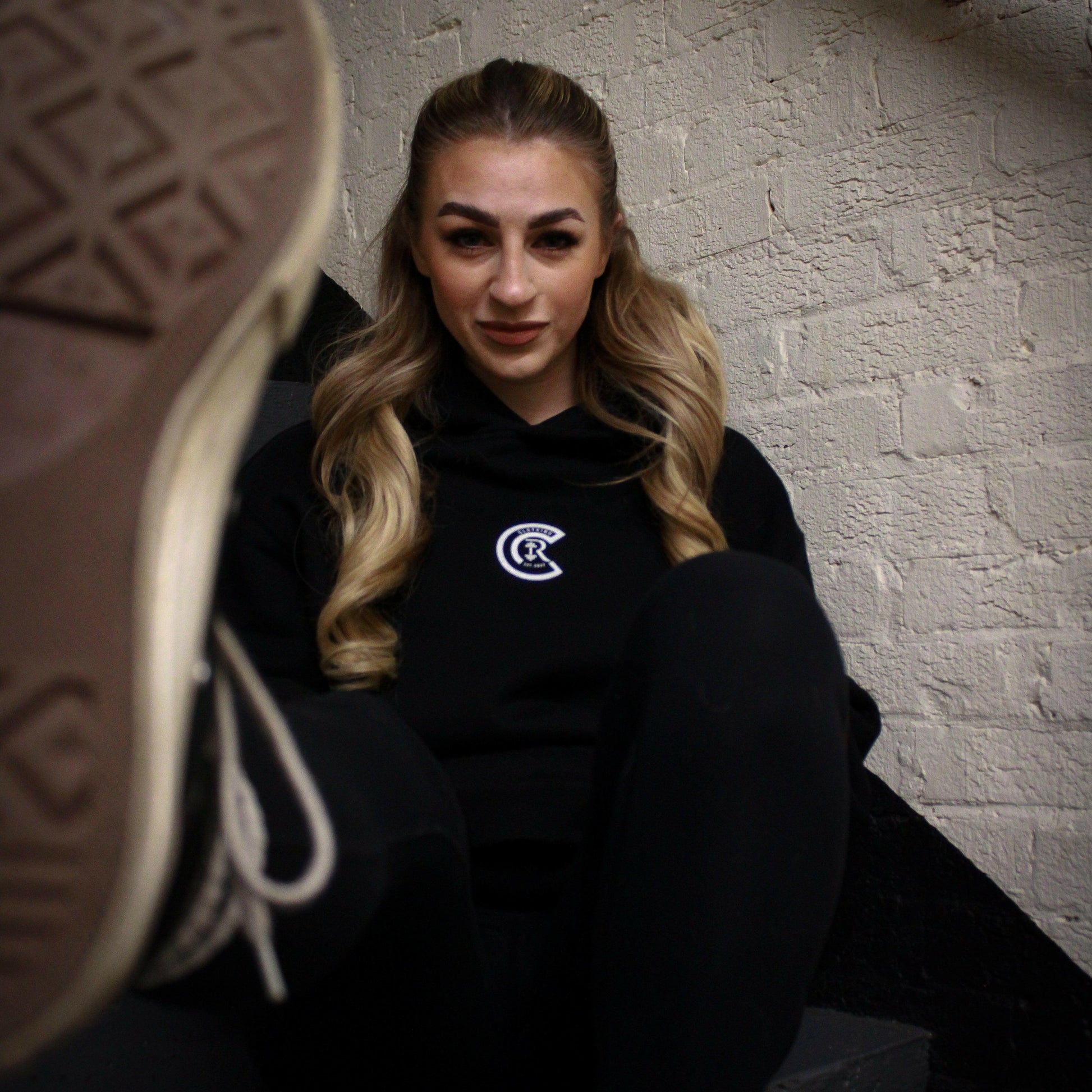 Chase Results clothing brand, based in Norfolk Norwich, features a confident blonde woman wearing the Empower Confidence hoodie. In a dimly lit Norfolk stairwell. The hoodie, designed for both comfort and style, reflects strength and empowerment, making it the perfect choice for those looking to embrace their inner power