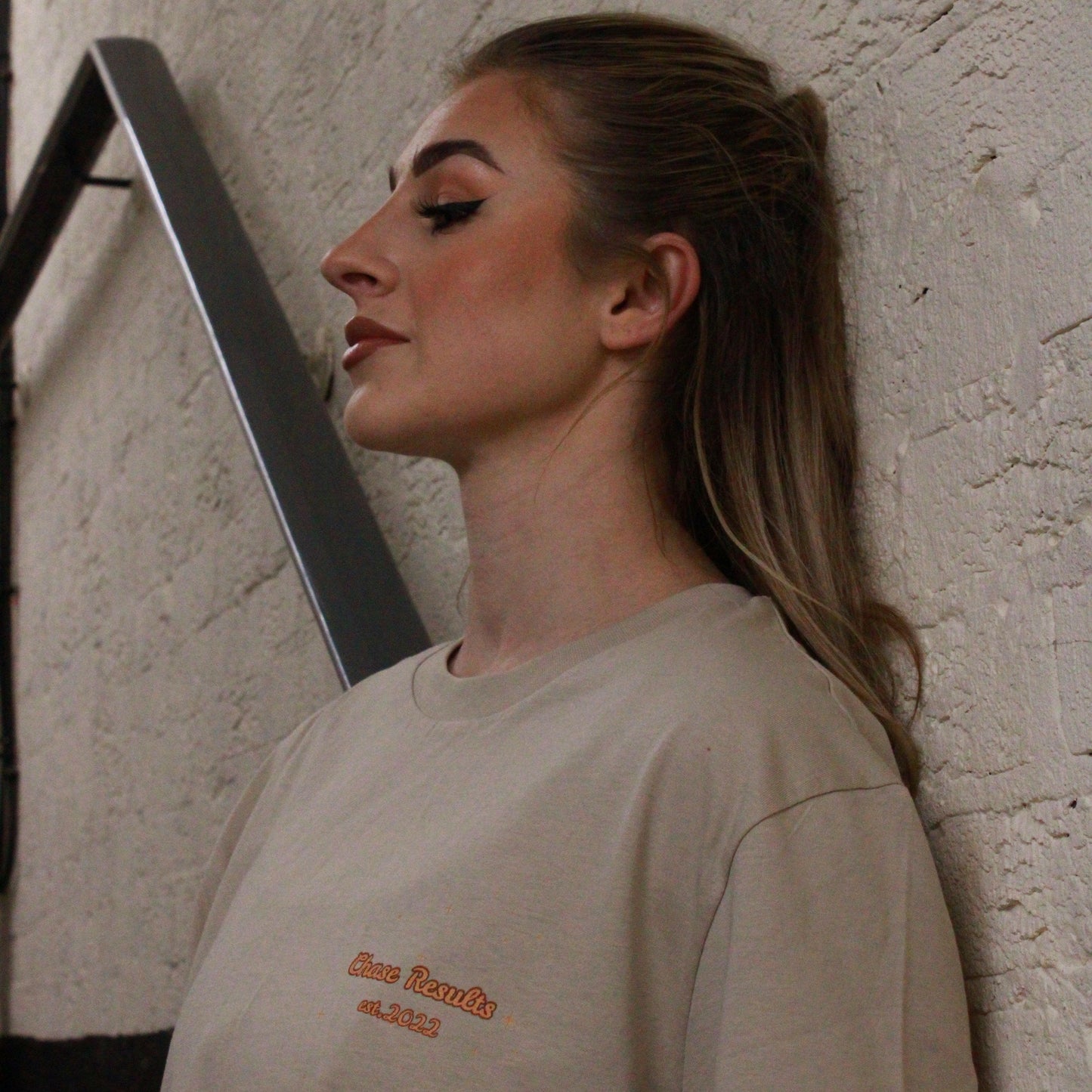 A woman descends the stairs at Great Yarmouth wearing a beige Pump Espresso T-Shirt by Chase Results Clothing, featuring a cartoon coffee cup character. Metal railings frame her path, while a caution sign above ensures safety along her way.