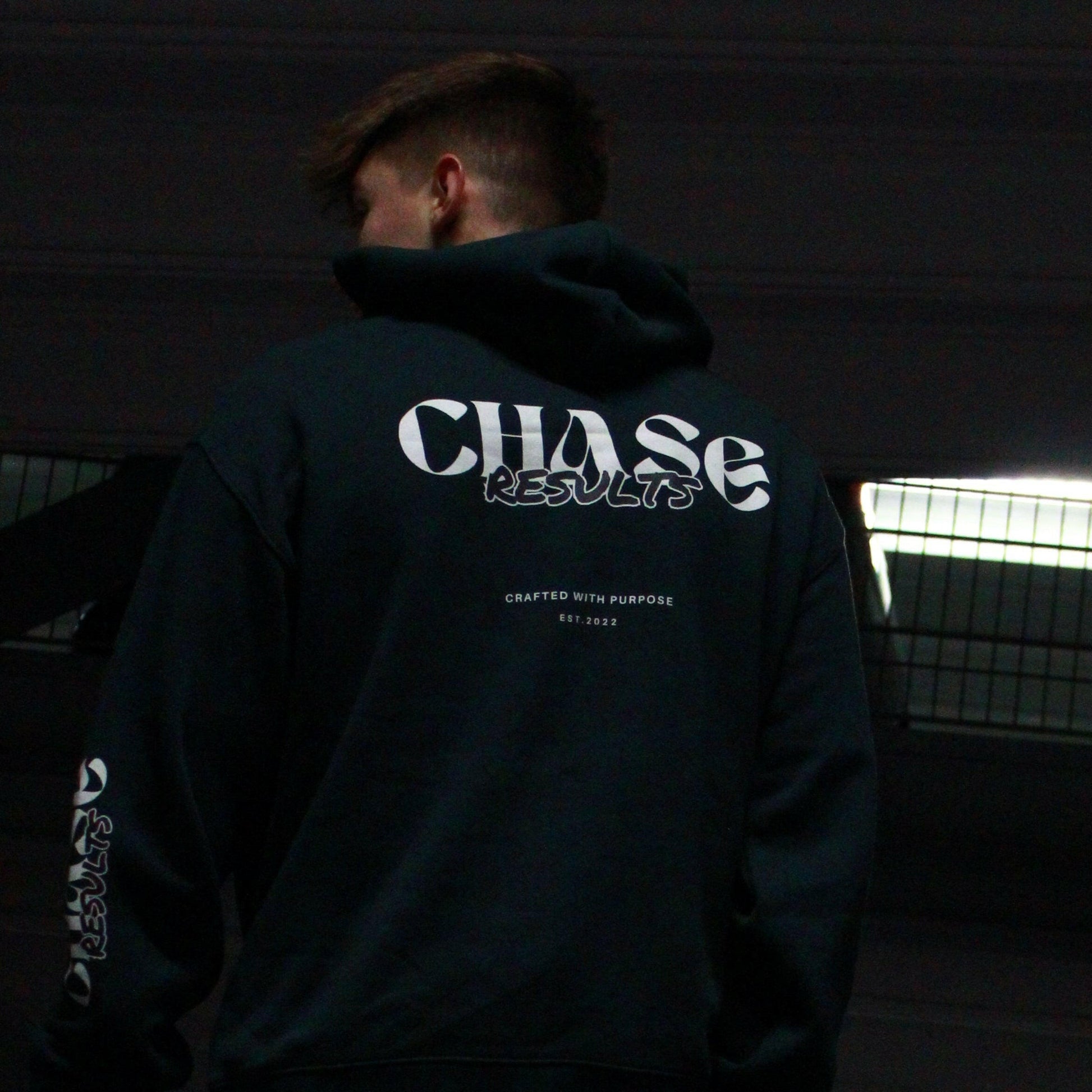 In a dimly lit Norfolk carpark, a person is seen with their head slightly down and to the side, They wear the Chase Results oversized hoodie by Chase Results Clothing, its bold graphic design enhancing the scenes artistic feel over just any other backdrop. Perfect for those gym lovers, It's Gym wear you can wear anywhere.