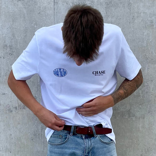 Person wearing a white t-shirt with logos against a concrete wall