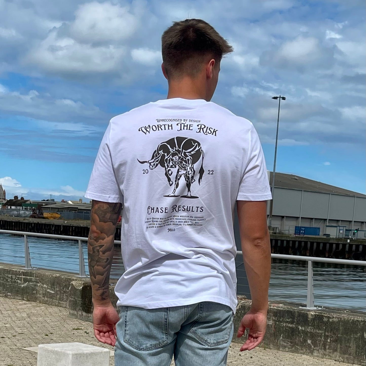 Person wearing a white t-shirt with a graphic design by a waterfront
